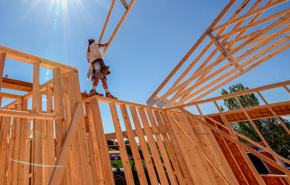 Construction worker standing on the wooden frame of a building in progress and placing rafters for the roof.
