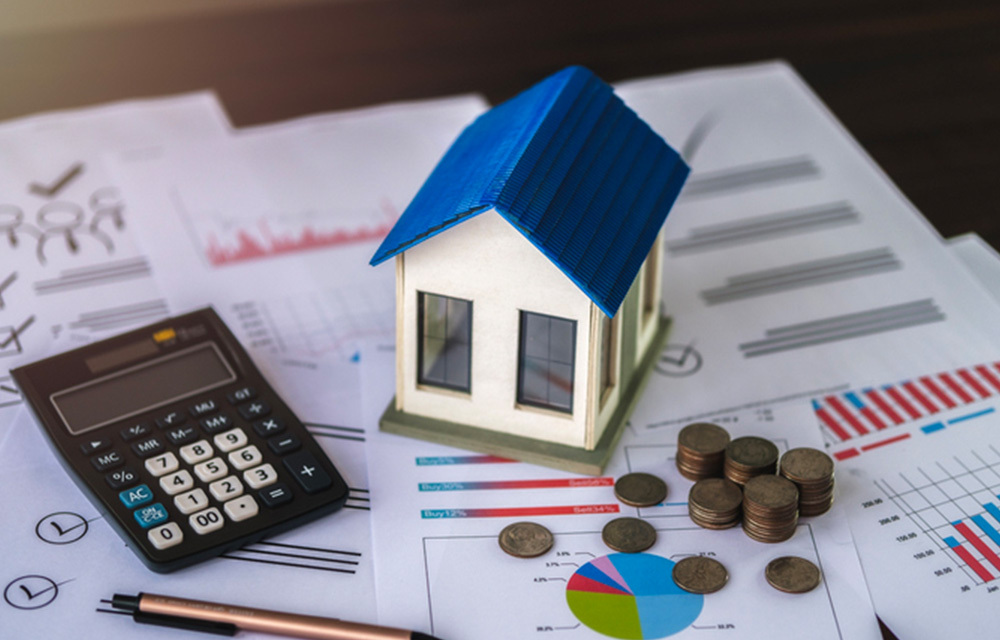 Small model house sitting and coins sitting on top of paper with charts.
