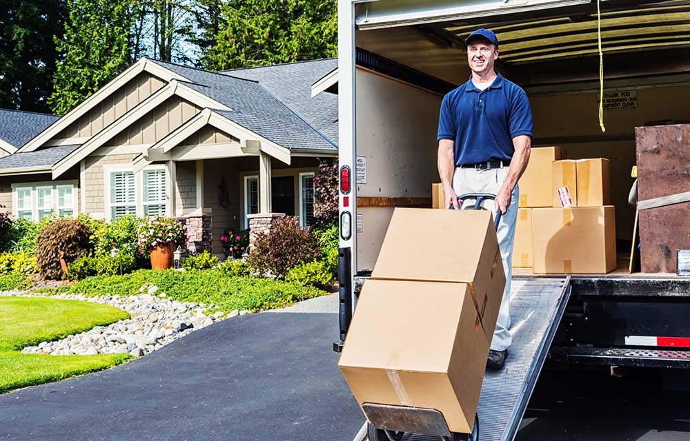 Delivery man unloading truck, walking cardboard boxes down ramp on a hand truck.