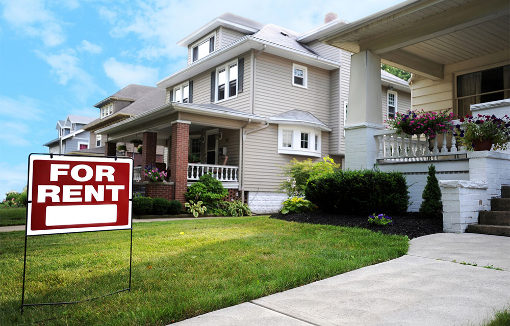For rent sign in the yard of a medium-sized house.