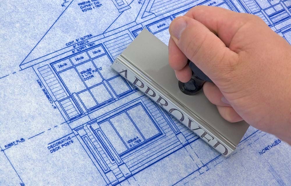 An approval being stamped onto a blueprint for a single-family house.