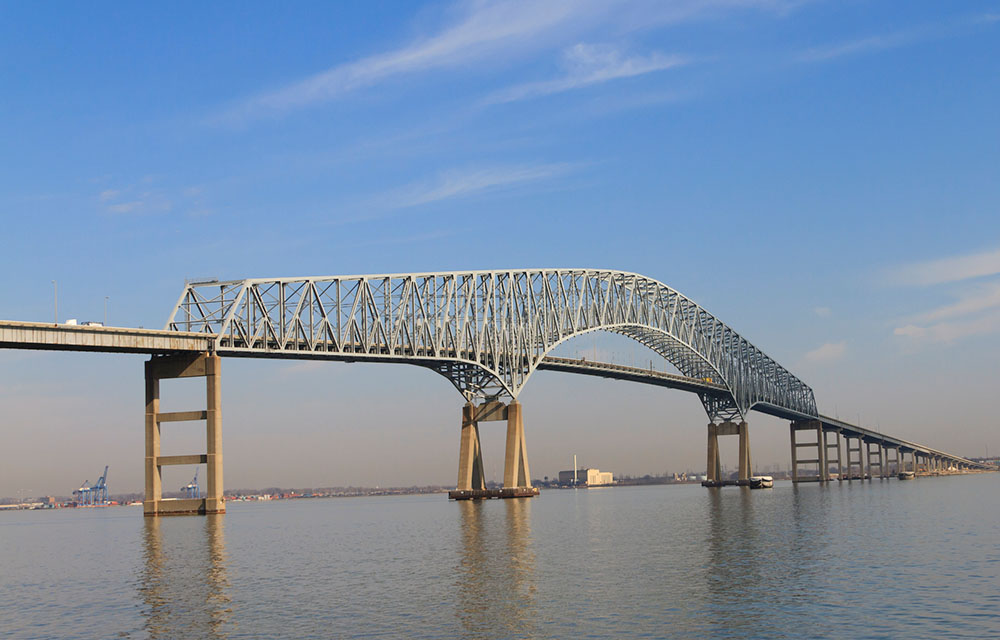 The Francis Scott Key Bridge during the daytime with a port seen distantly in the background.