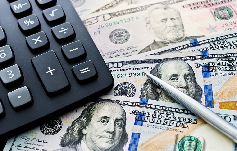 Assortment of cash with a calculator and pen laying on top.