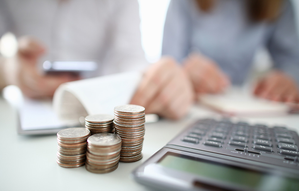 Stacks of quarters and a calculator in the foreground as accountants work in the background.