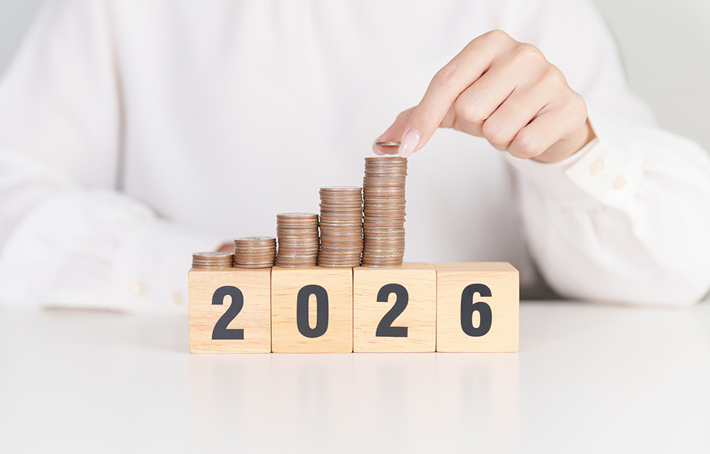 Person stacking quarters on top of wooden blocks arranged to read "2026."