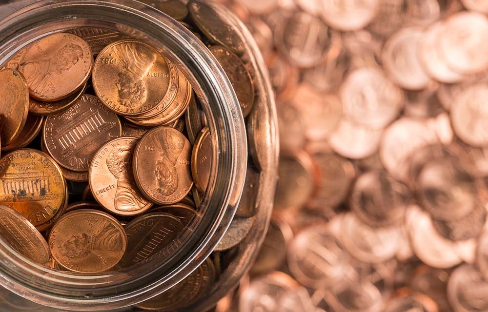 A jar of pennies sitting on top of a pile of pennies.