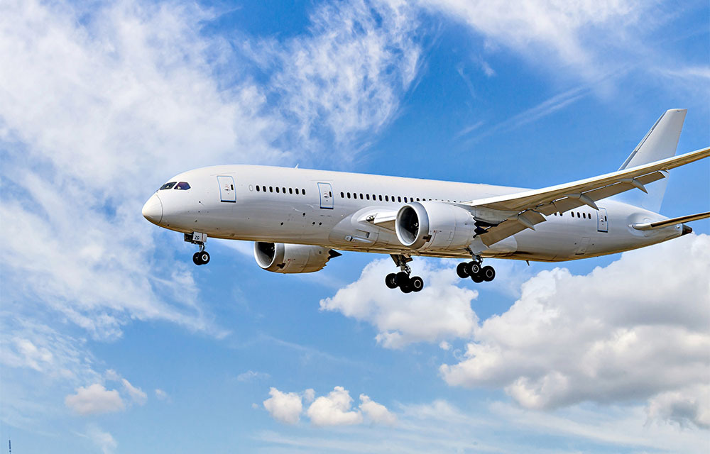 Boeing 787-8 Dreamliner passenger plane landing at the airport, under a blue sky with white clouds.
