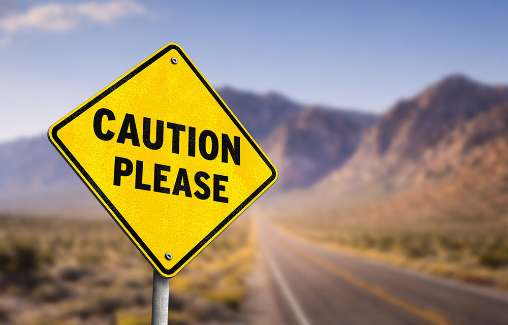 Yellow caution sign with a desert background behind it.