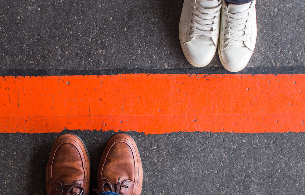 Close-up of two pairs of feet on opposite sides of a line in the road