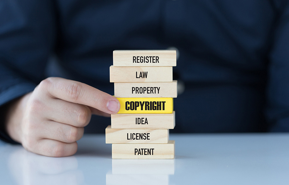 Stacked wooden blocks each labelled with terms like "law," "property," and "patent," with a yellow block that reads out "copyright."