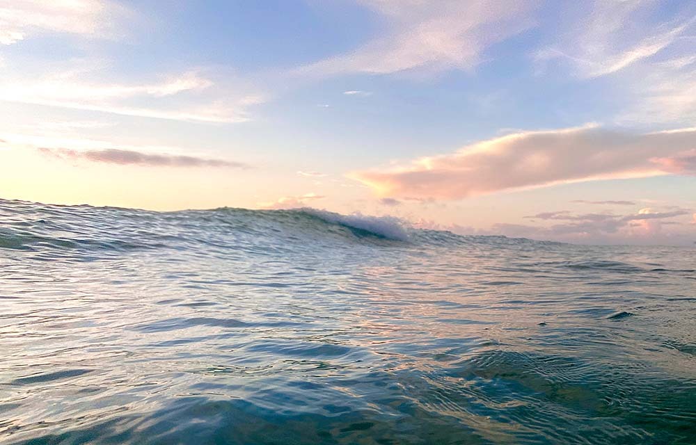 Ocean wave at sunrise in a tropical sea with reflections of the sky