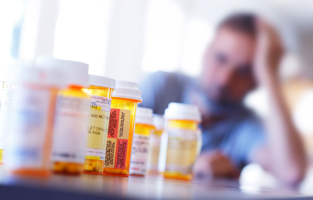 Prescription drugs in the foreground and a man in the background staring at them