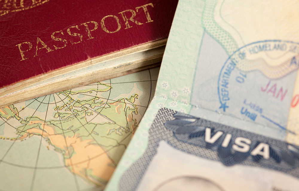 Close up on a couple passports laying on a vintage map with one open to show a visa.