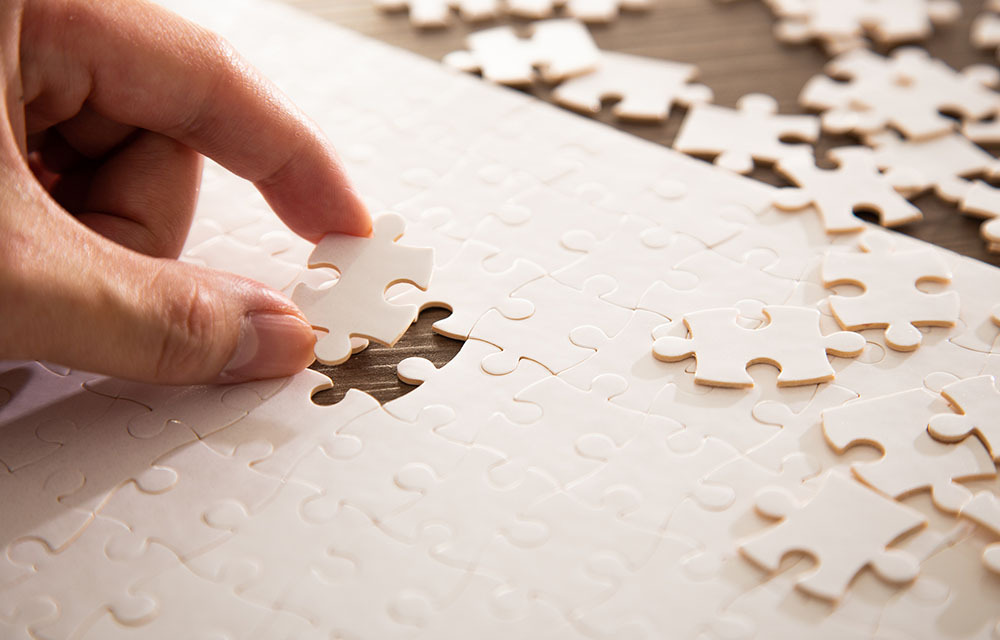 Close up of a hand placing the final puzzle piece into a white jigsaw puzzle.