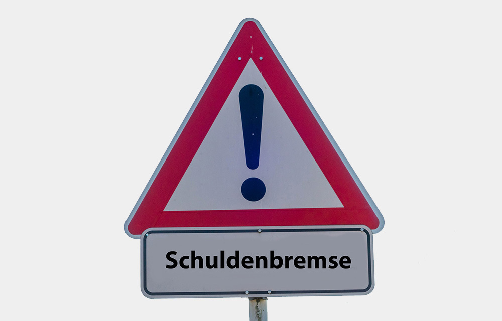 Road sign of a triangle with an exclamation point and the word Schuldenbremse at the bottom.