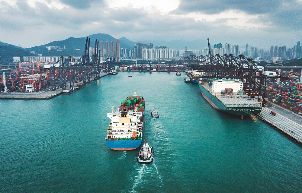 Container ship approaching a port attached to a city with large buildings.