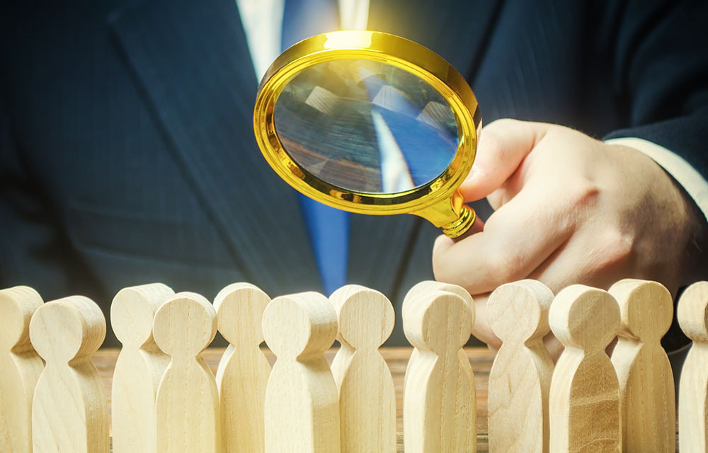 Man looking through a magnifying glass at wooden people-like figures.