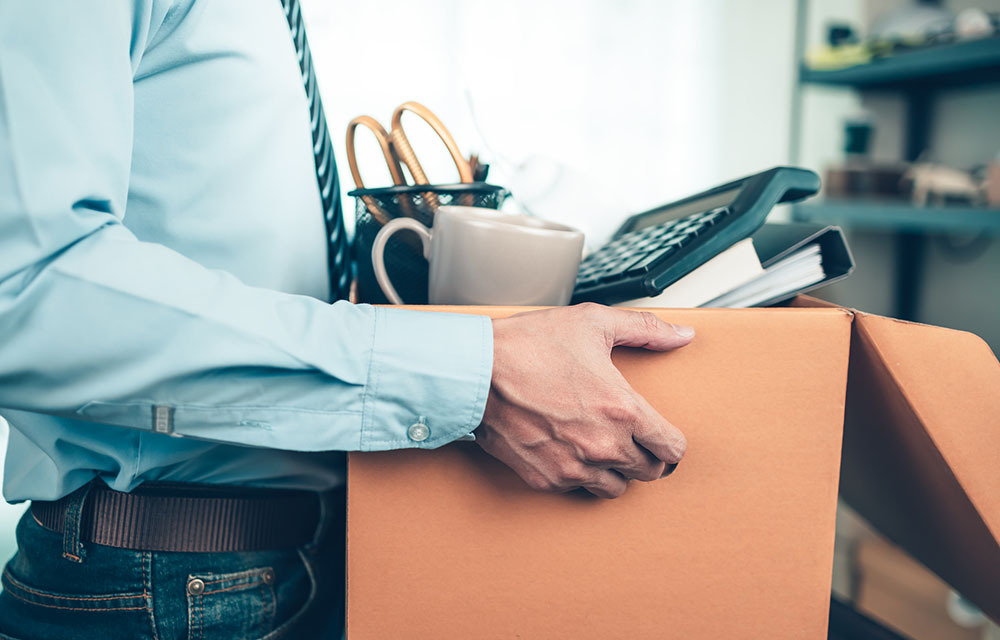 Man in business attire carrying a box of his office belongings.