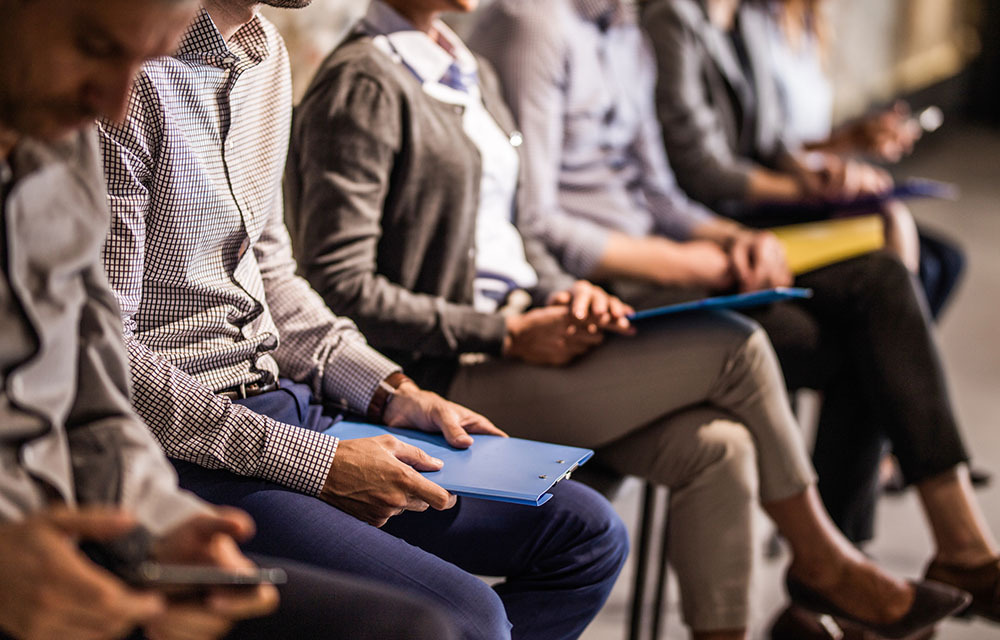 Group of unrecognizable business people waiting for a job interview. Focus is on man with blue clipboard.