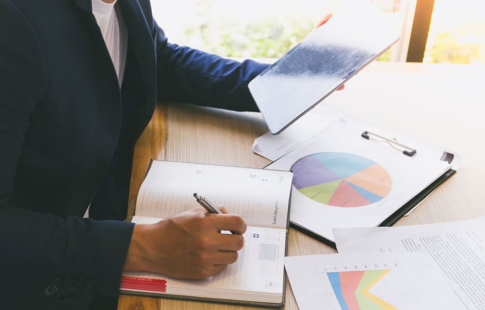 A business person reviewing charts in a notebook and tablet