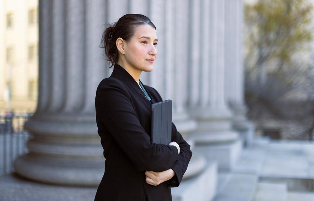 Woman in business attire hugging her tablet while deep in thought.