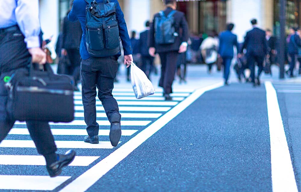 A busy street crossing with men in suits, backpacks, and with suitcases heading to work.