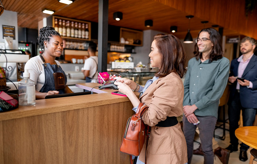 Customers lining up to make a purchase from the barista in a coffee shop.