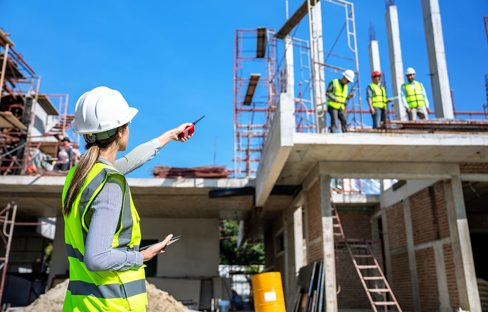 Foreman is directing construction workers in reflective vests and hardhats who are standing on an unfinished structure.