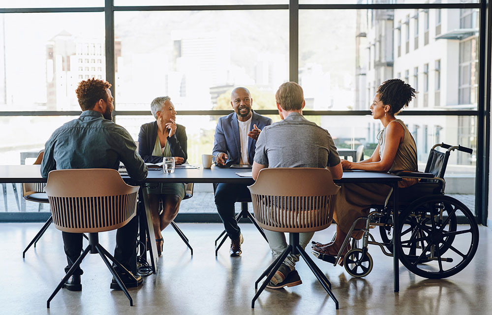 Employees meeting around a table as one employee, who uses a wheelchair, advocates for the importance of inclusion.