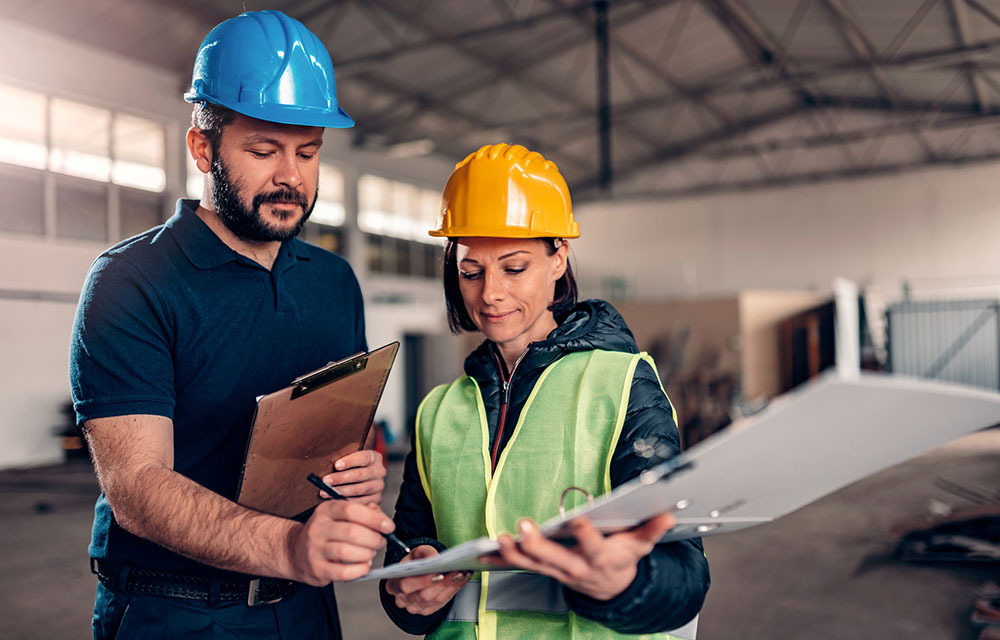 Production line workers signing document in industrial factory while wearing hardhats.