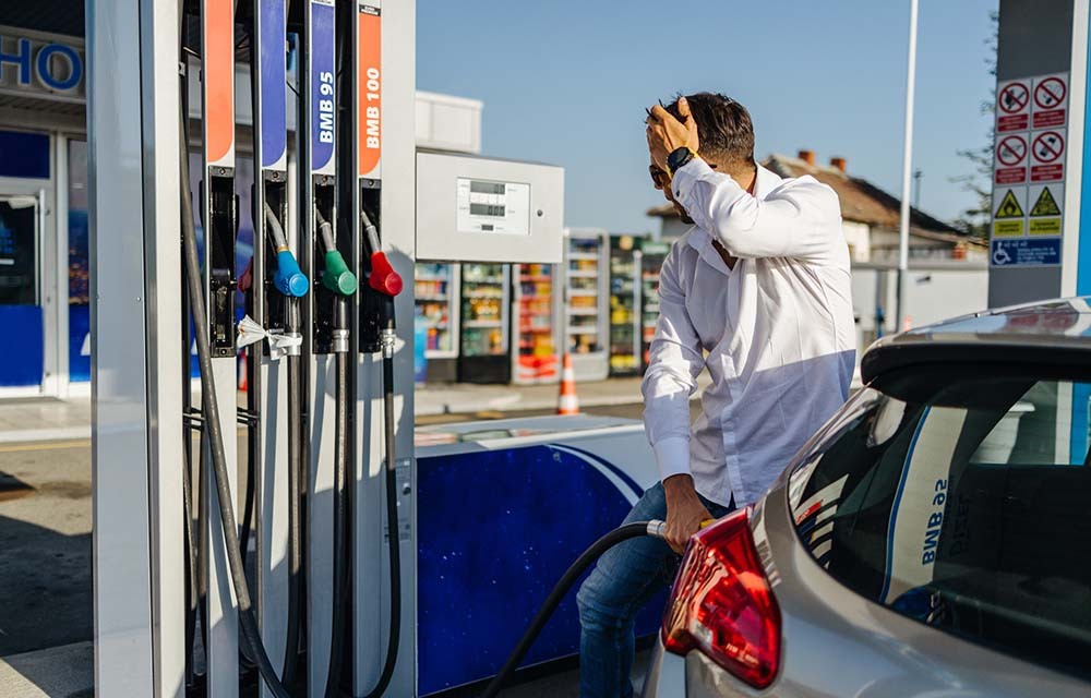 Frustrated man with his hand on his head as he refuels his car.