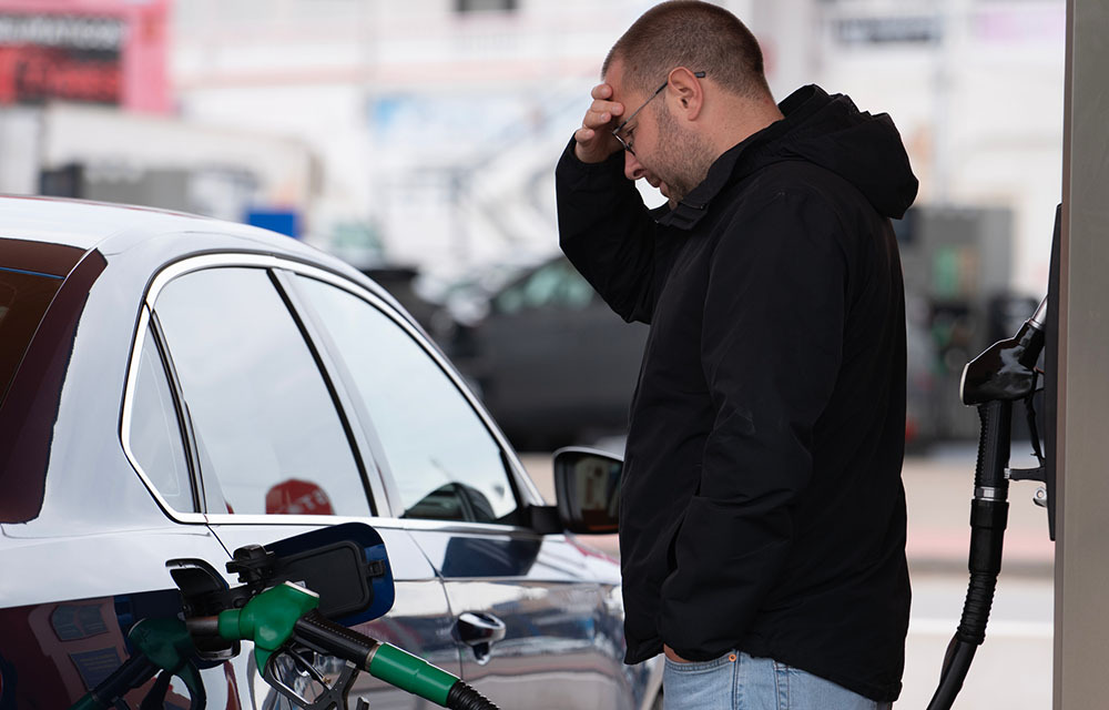 Frustrated man with his hand on his head as he refuels his car.