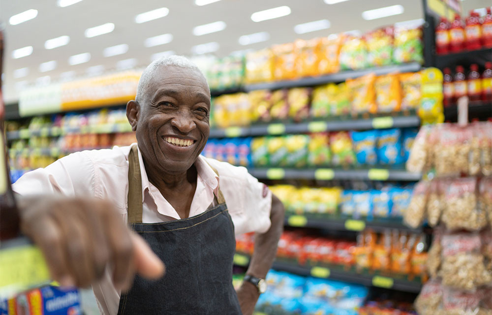 A smiling grocery store clerk with an apron on standing in front of merchandise.