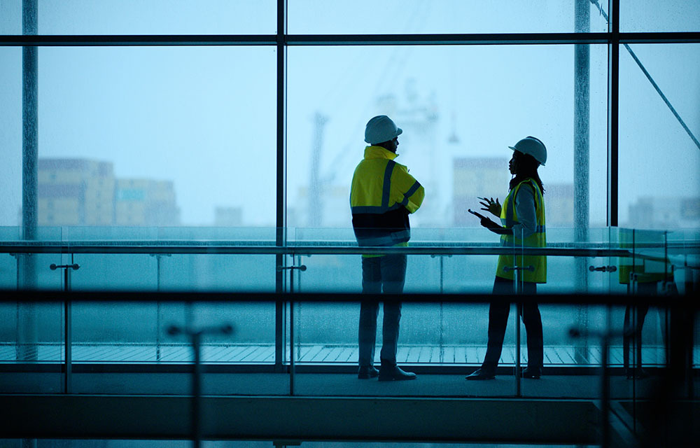 Construction foremen in high visibility wear and helmets evaluating glass windows.