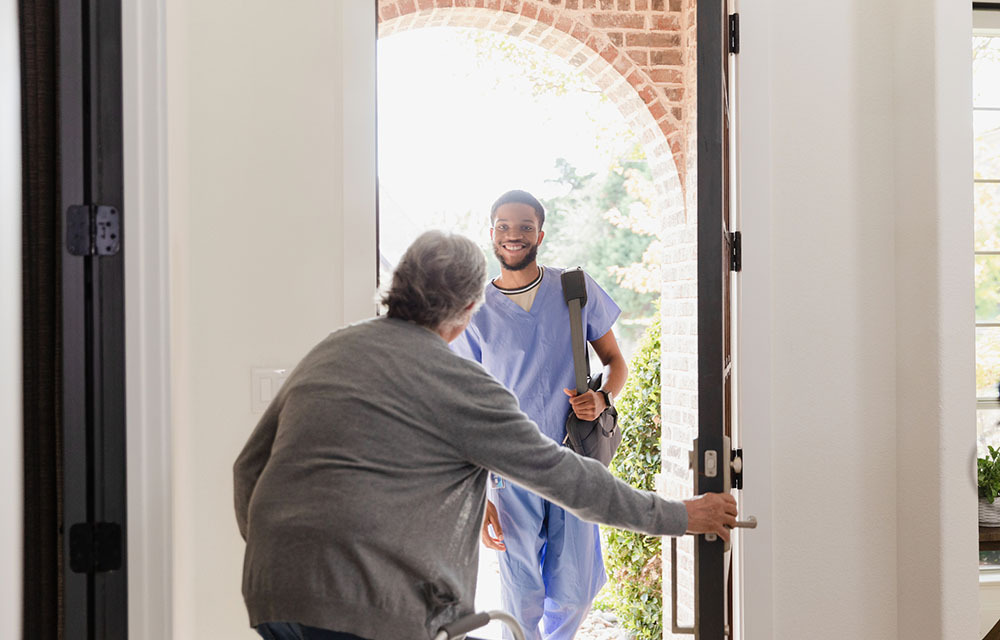 Senior man with a mobility walker opening the front door of his home to let in his physical therapist.