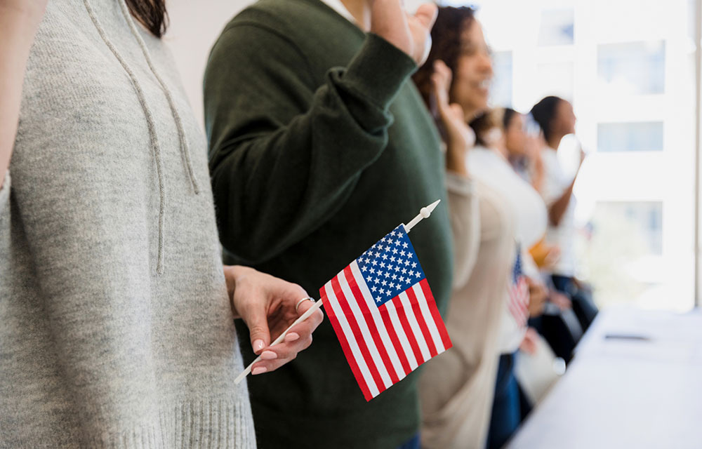Line of people raising hands to say pledge while one holds small American Flag.