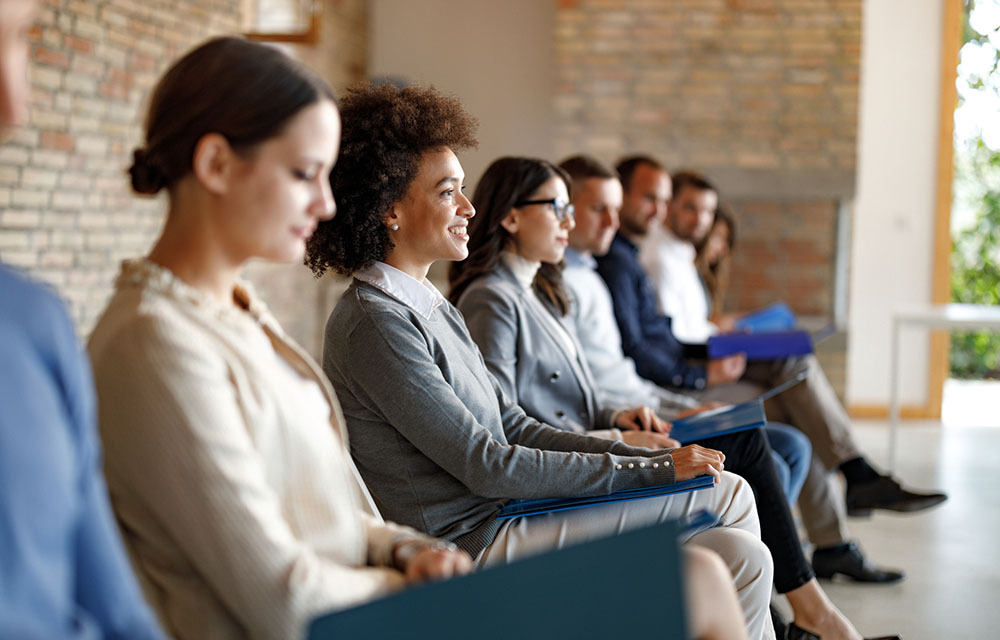 Group of people in business casual outfits sitting in a waiting room for their job interview.