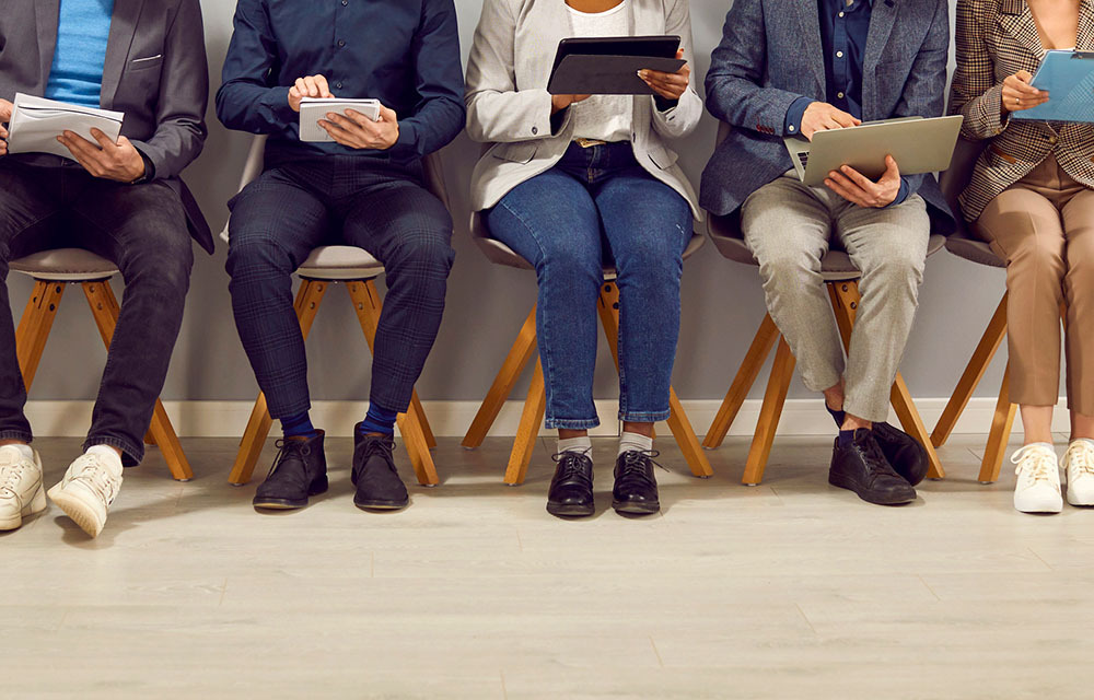 Job applicants waiting in a line of chairs as they review their notes.