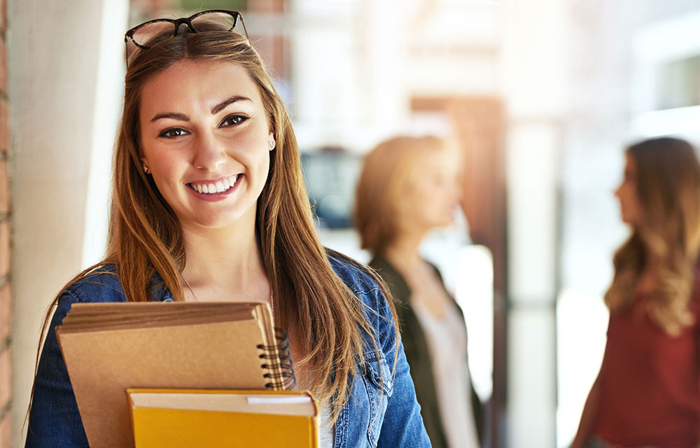 young woman smiling while holding books