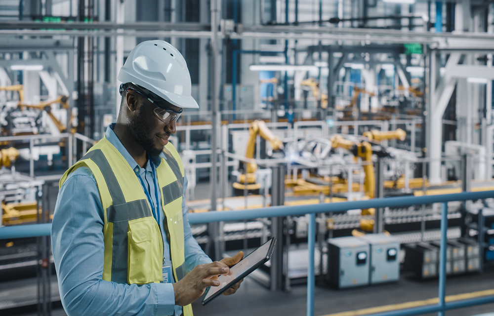 Man with safety vest examining his tablet inside of a factory.