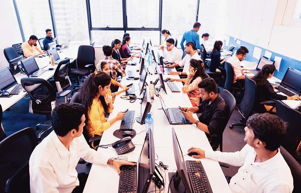 Office with many IT workers sitting in front of computers.