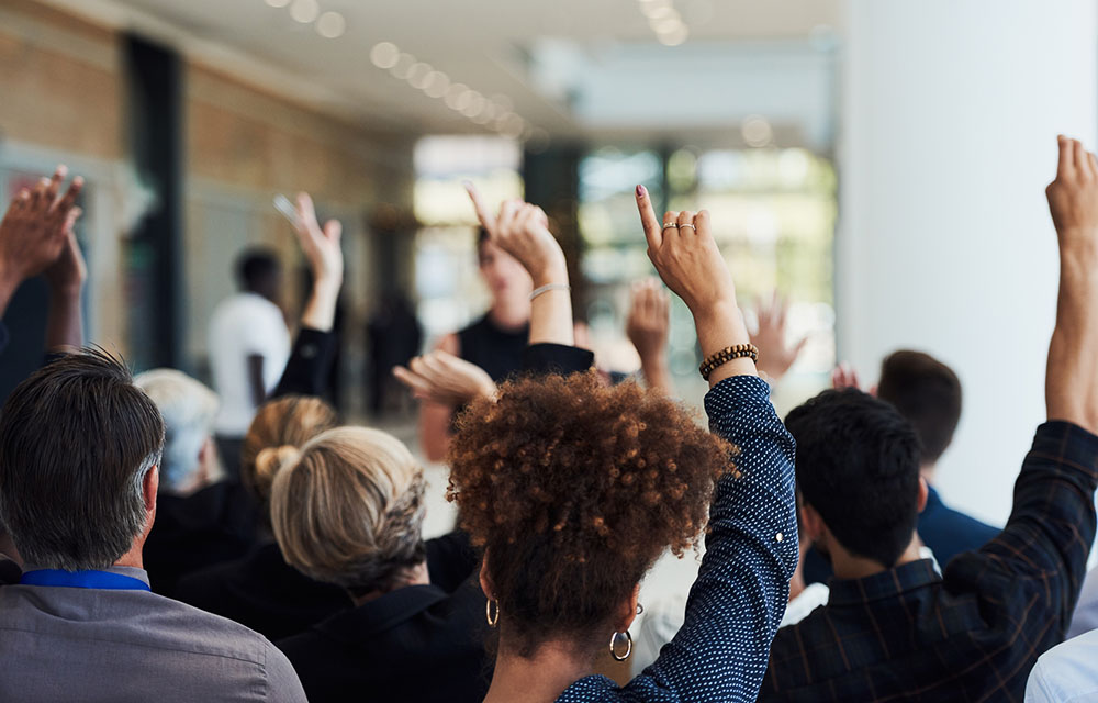 Group of businesspeople raising their hands to ask questions during a conference