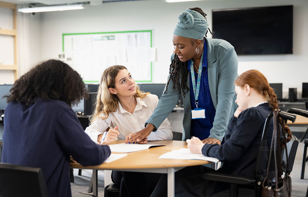Young adults sitting around a table and discussing notes as an instructor offers input.