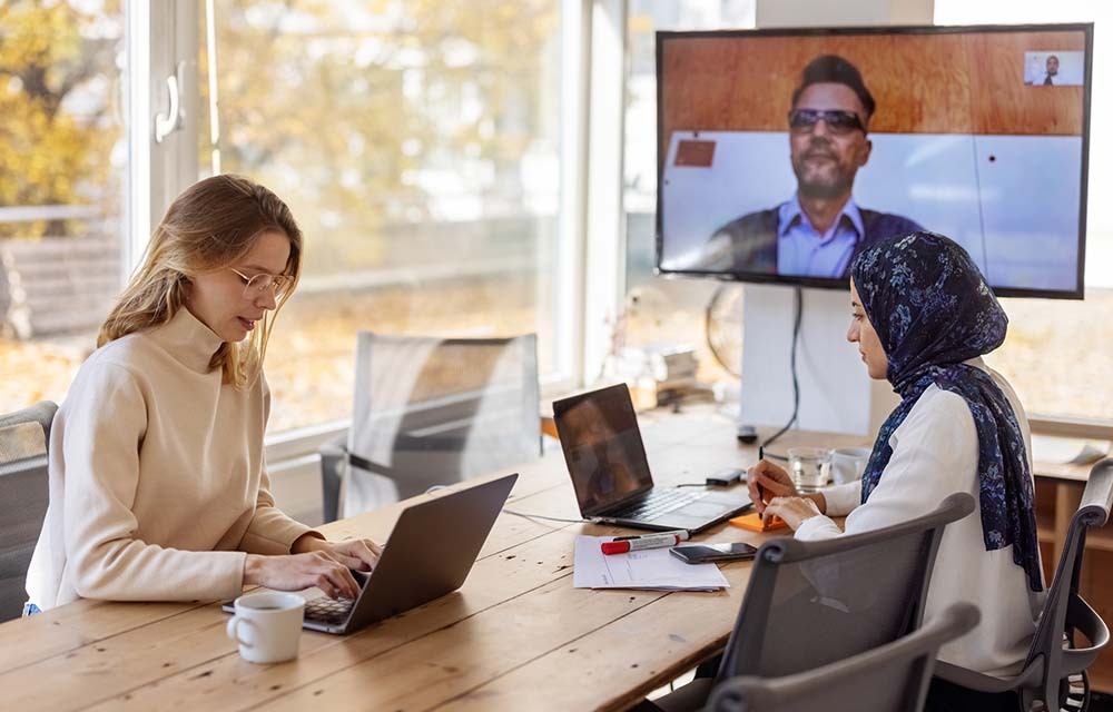 Team planning in a conference room with a colleague on a hybrid video call