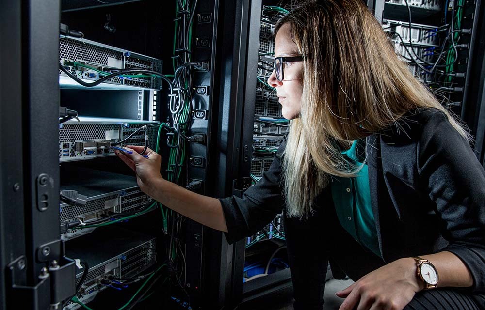 A woman network engineer working on equipment in a wiring closet.