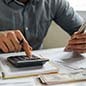 Man at a desk using a calculator and holding paper money in his hand