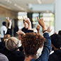 Group of businesspeople raising their hands to ask questions during a conference