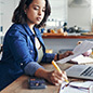 Woman working with a laptop, pencil, paper and calculator in kitchen at home