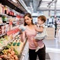 Woman holding toddler examines groceries at a grocery store
