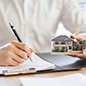 Man writing a real estate contract and holding a model house